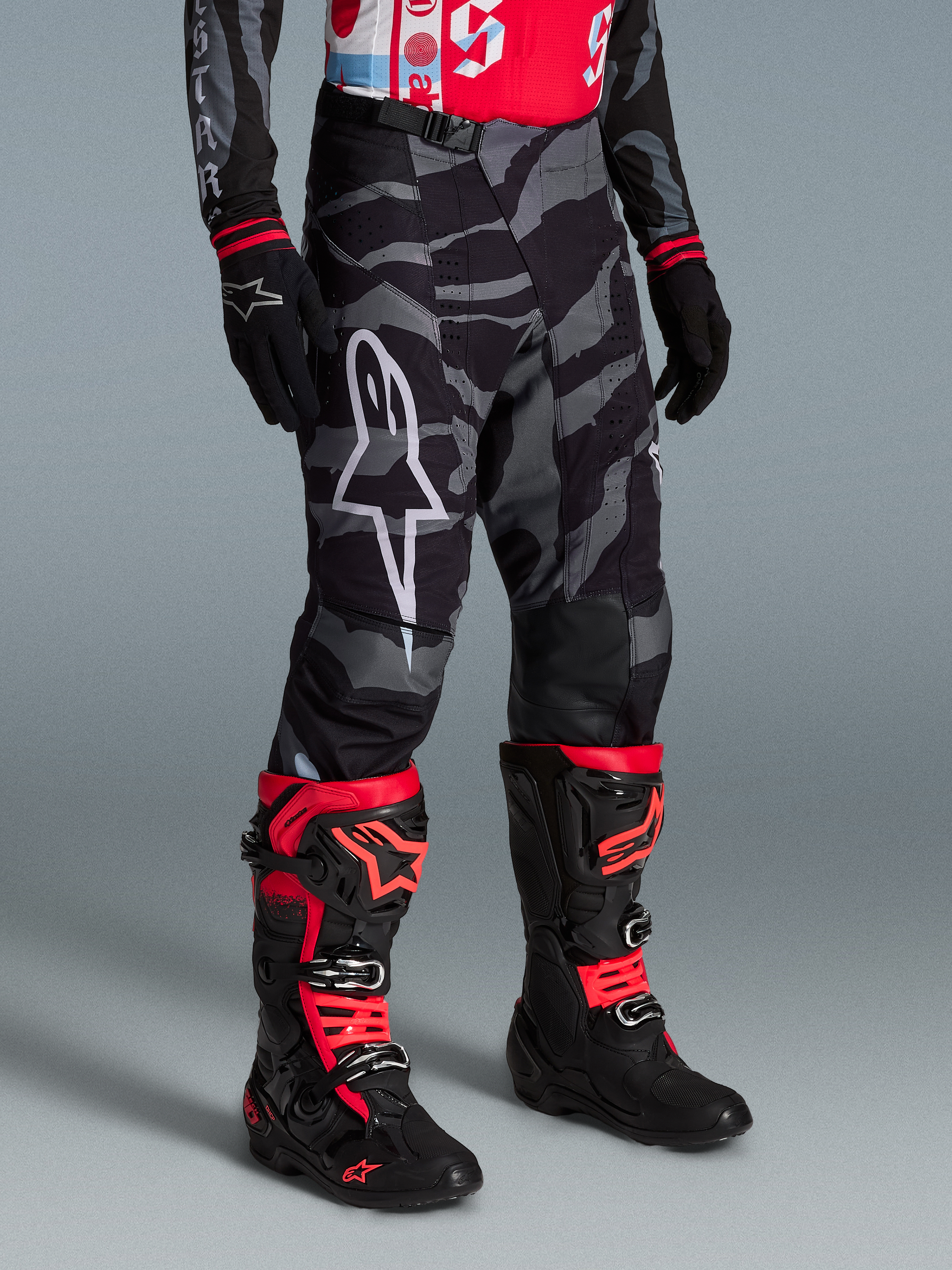 Beperkte Oplage Techstar Beast Coast Broek, zwart-grijs camo, wit logo, gedragen met rood-zwarte motorlaarzen.