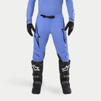 Alpinestars 2024 Supertech Dade crossbroek, motorcross broek, lichtblauw, met grote zwarte Astars-logo's op de dijen, zwarte gesp in de taille, gedragen met zwarte motorcrosslaarzen en bijpassende blauwe top, professionele off-road racekleding