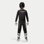 Motorcrosser in volledige race-uitrusting, Alpinestars 2024 Fluid Graphite Pants in zwart en zilver, zwarte jersey met lange mouwen en zilveren branding, zwarte helm met crossbril, wit-zwarte laarzen en handschoenen, gecoördineerde outfit voor motorcross