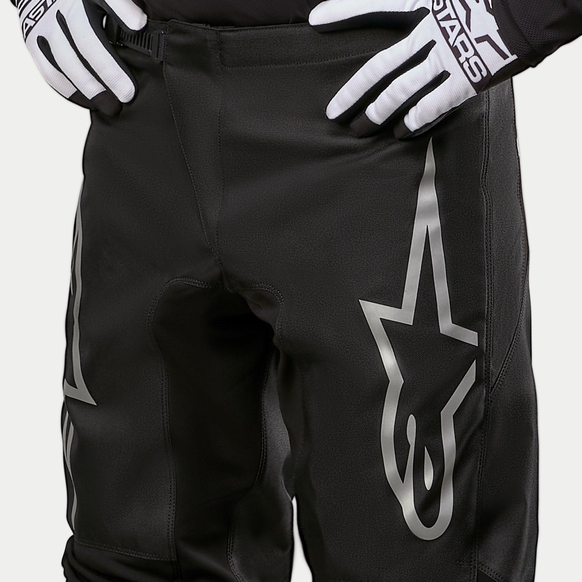 Alpinestars 2024 Fluid Graphite crossbroek, motorcross broek, zwart en zilver, detailopname van de bovenbenen en de taille, met een groot zilveren ster-logo op het been, gedragen met zwart-witte racehandschoenen