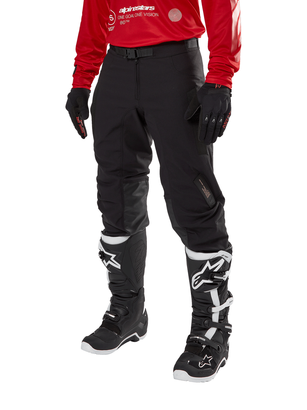Alpinestars Techdura broek, zwarte off-road motorbroek, gedragen met een rode jersey met lange mouwen en zwart-witte motorcrosslaarzen, robuuste stretch polyamide constructie, leren knieverstevigingen aan de binnenzijde en een verstelbare riem voor enduro rijden.