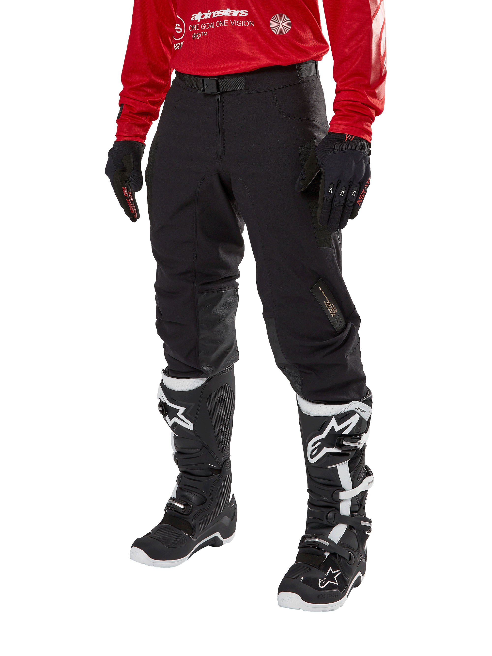 Alpinestars Techdura broek, zwarte off-road motorbroek, gedragen met een rode jersey met lange mouwen en zwart-witte motorcrosslaarzen, robuuste stretch polyamide constructie, leren knieverstevigingen aan de binnenzijde en een verstelbare riem voor enduro rijden.