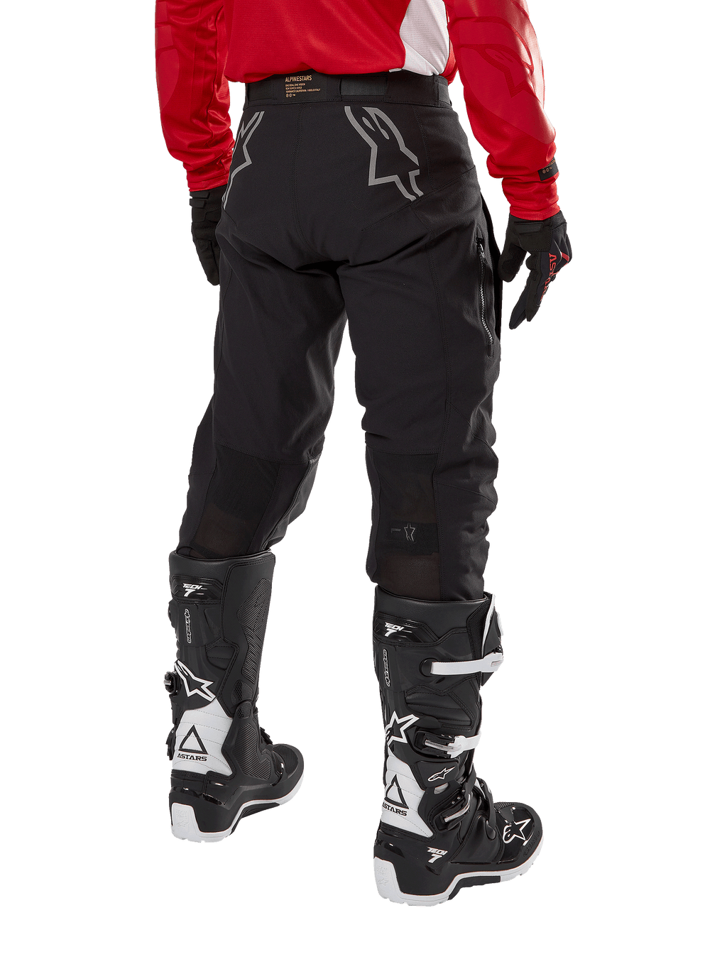 Alpinestars Techdura broek, off-road endurobroek, zwart, achteraanzicht met grijze sterlogo's op het zitvlak, gedragen met een rood jersey met lange mouwen en zwart-witte Tech 7 laarzen, robuuste textielconstructie voor adventure rijden