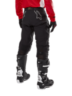 Alpinestars Techdura broek, off-road endurobroek, zwart, achteraanzicht met grijze sterlogo's op het zitvlak, gedragen met een rood jersey met lange mouwen en zwart-witte Tech 7 laarzen, robuuste textielconstructie voor adventure rijden