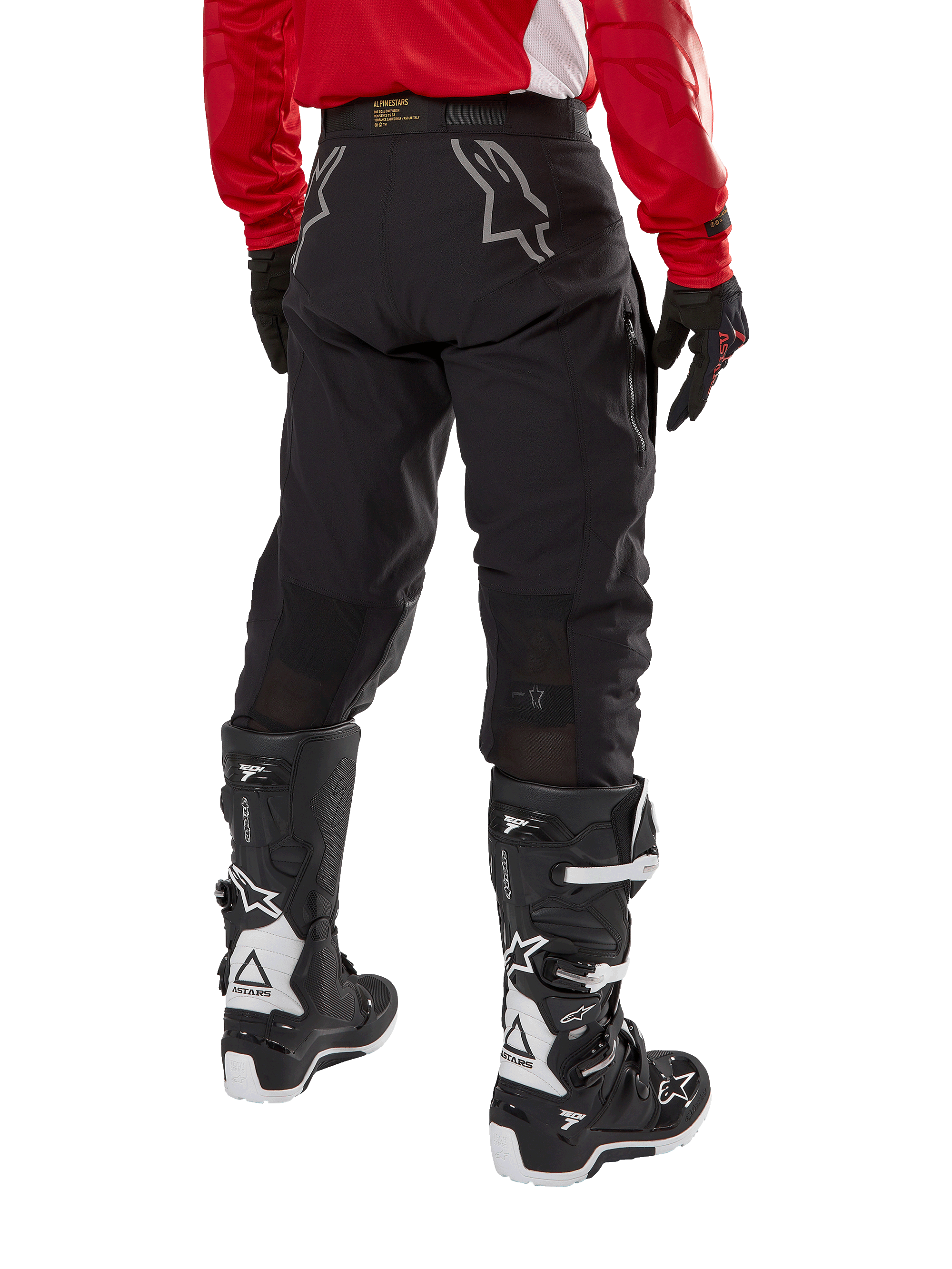 Alpinestars Techdura broek, off-road endurobroek, zwart, achteraanzicht met grijze sterlogo's op het zitvlak, gedragen met een rood jersey met lange mouwen en zwart-witte Tech 7 laarzen, robuuste textielconstructie voor adventure rijden
