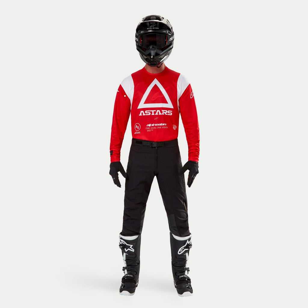 Alpinestars Techdura broek, enduro- en off-roadbroek, zwart, gedragen met een rood en wit Astars jersey met lange mouwen, zwarte helm en zwart-witte laarzen, voorzien van een robuuste stretch polyamide constructie en technische panelen voor off-road rijden.