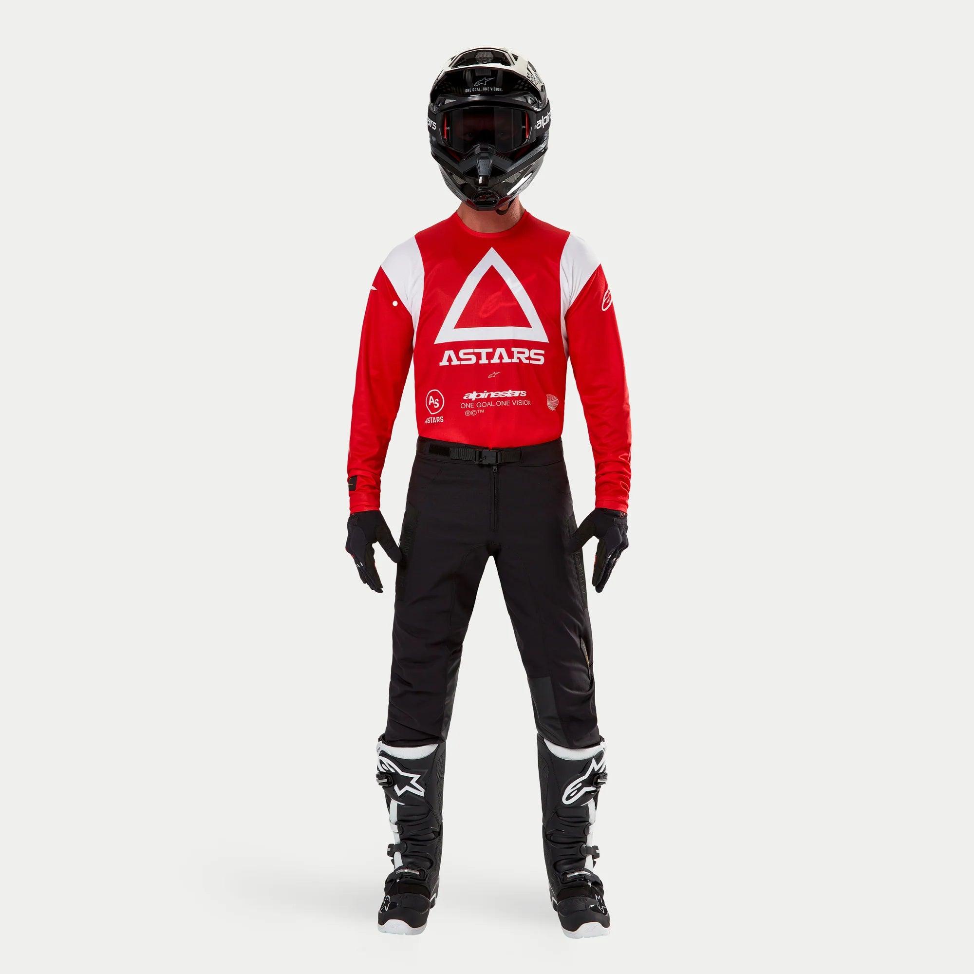 Alpinestars Techdura broek, enduro- en off-roadbroek, zwart, gedragen met een rood en wit Astars jersey met lange mouwen, zwarte helm en zwart-witte laarzen, voorzien van een robuuste stretch polyamide constructie en technische panelen voor off-road rijden.