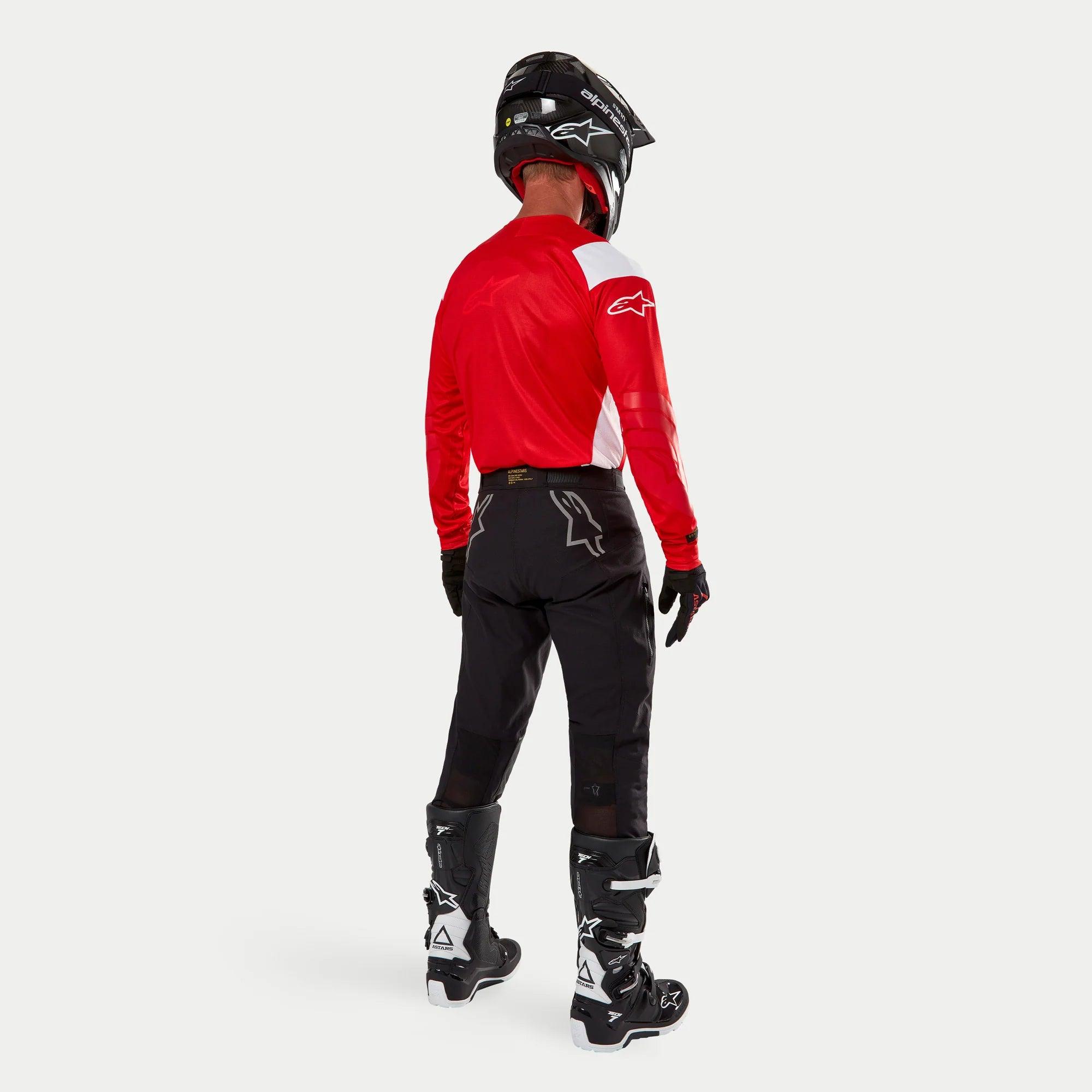 Alpinestars Techdura broek, enduro off-road broek, zwart, achteraanzicht gedragen door een rijder met een rood-wit shirt en zwart-witte laarzen, voorzien van witte sterlogo's op de achterkant en een duurzame technische stretchconstructie.