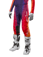 Alpinestars 2024 Techstar Pneuma crossbroek, motorcross broek, paars met oranje en blauw kleurverloop, witte logo's, persoon draagt de broek in combinatie met witte motorcrosslaarzen en handschoenen, sportieve off-road uitrusting