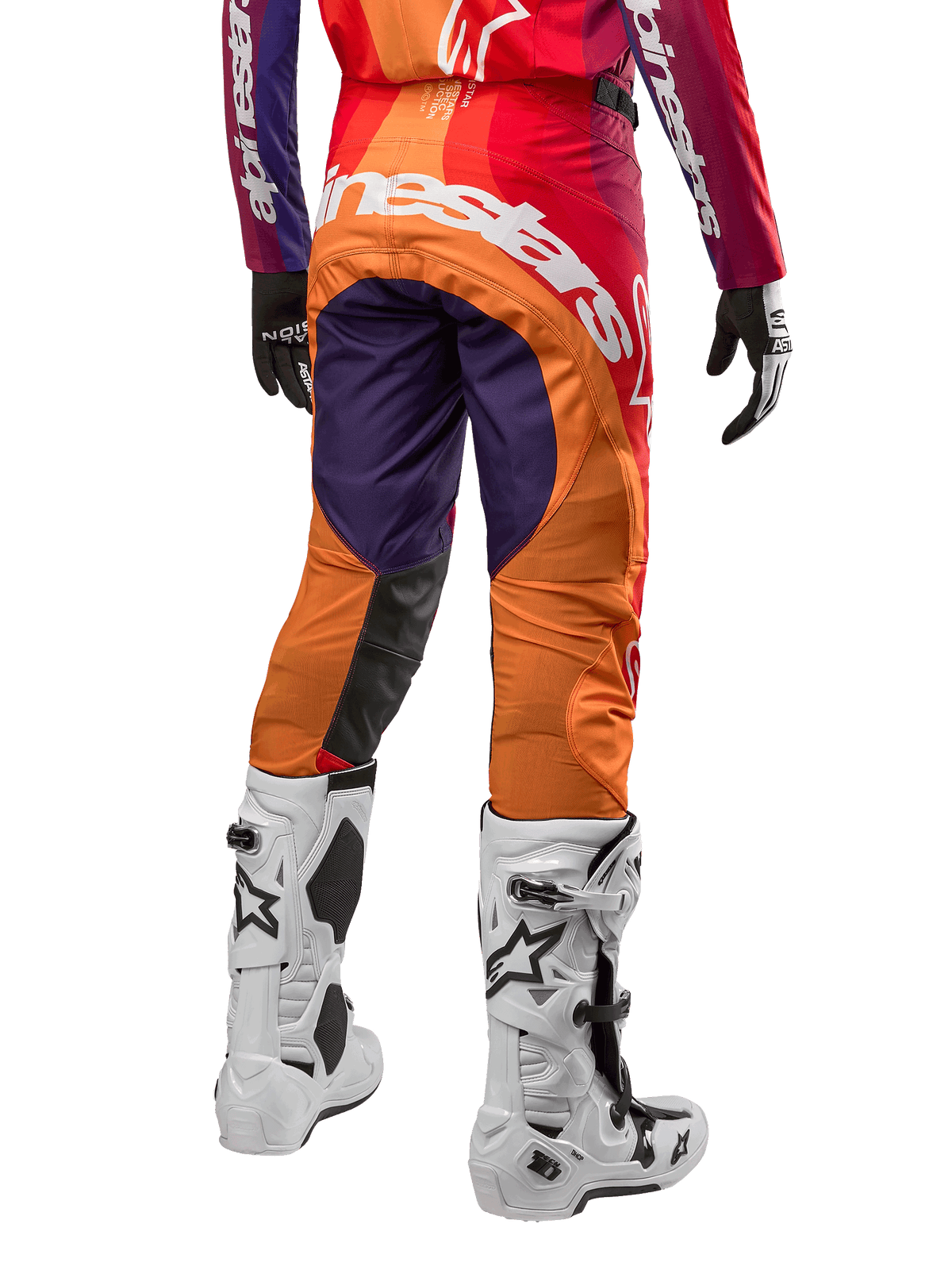 Alpinestars 2024 Techstar Pneuma crossbroek, motorcross broek, dieppaars met oranje en donkerblauw, groot wit logo op de achterkant, achteraanzicht van persoon in volledige uitrusting met witte motorlaarzen