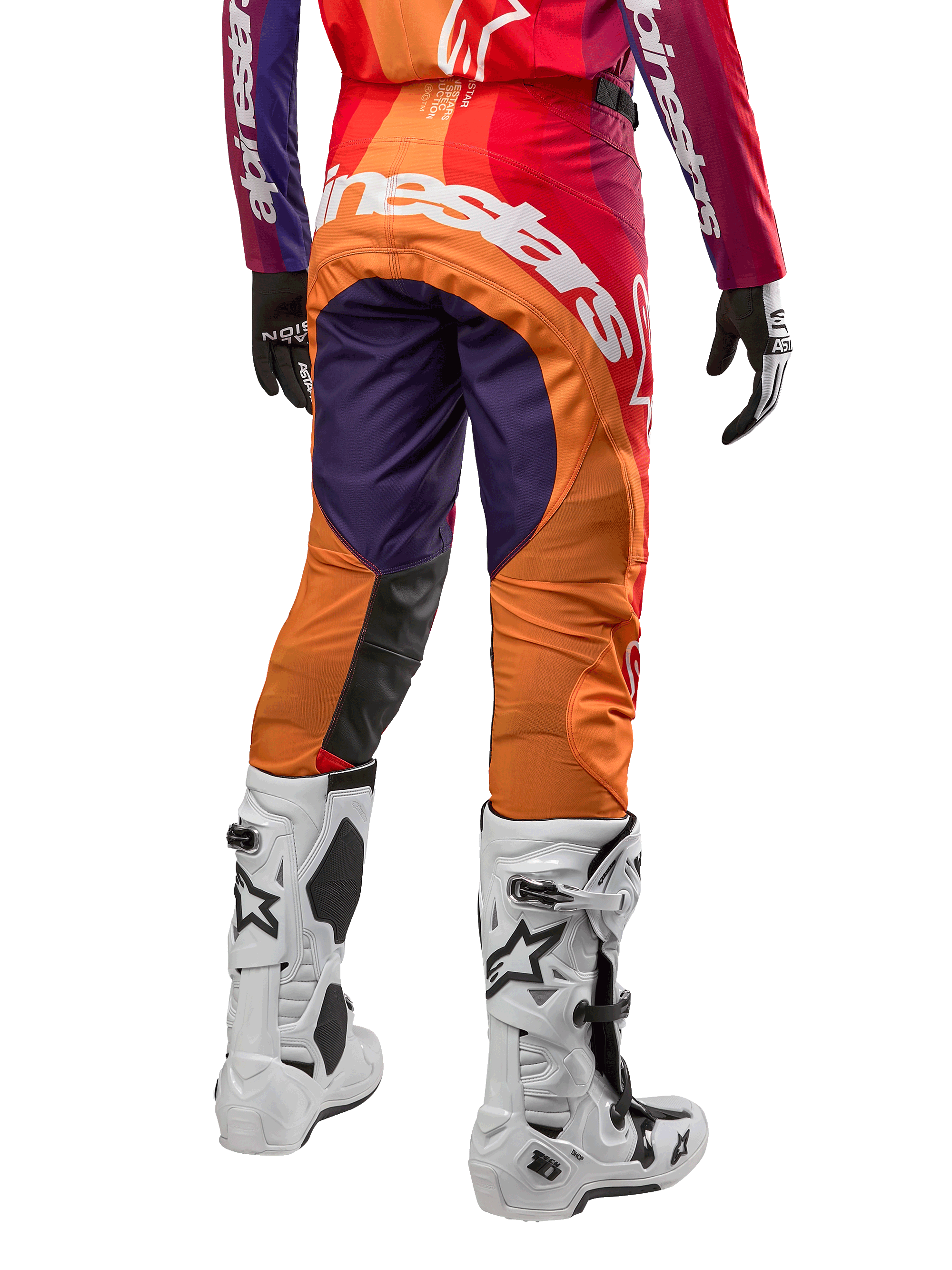 Alpinestars 2024 Techstar Pneuma crossbroek, motorcross broek, dieppaars met oranje en donkerblauw, groot wit logo op de achterkant, achteraanzicht van persoon in volledige uitrusting met witte motorlaarzen
