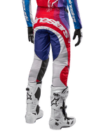 Alpinestars 2024 Techstar Pneuma crossbroek, motorcrossbroek, blauw mars rood wit, achteraanzicht gedragen met bijpassende jersey en witte laarzen, met opvallende witte branding op het zitvlak en veelkleurige panelen, professionele motorcross racekleding