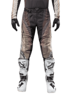 Alpinestars 2024 Techstar Pneuma broek, motorcrossbroek, donkerzand en grijs, gedragen met bijpassende jersey, zwarte handschoenen en wit-zwarte laarzen, voorzien van SX2 magnetische gesp en Astars-branding, duurzame off-road racekleding