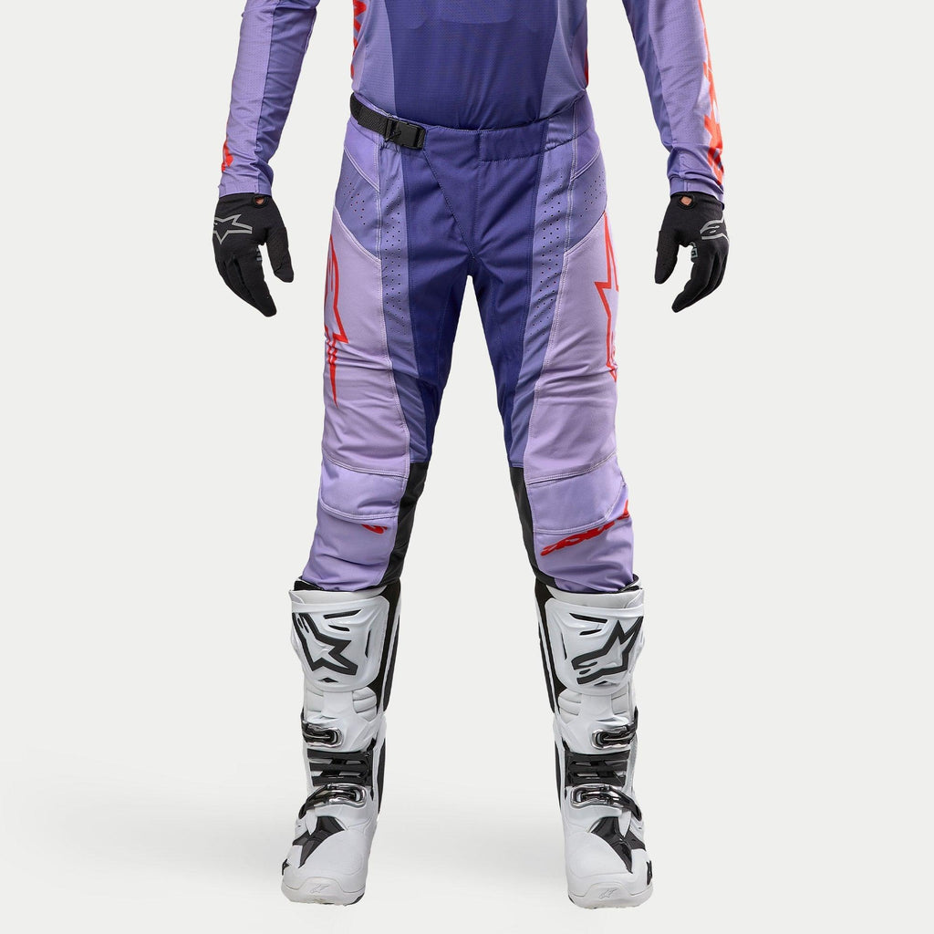 Alpinestars 2024 Techstar Ocuri crossbroek, motorcross broek, paars met felle oranje accenten, witte logo's, gedragen met witte motorcrosslaarzen en zwarte handschoenen, duurzame race-pasvorm voor motorcross