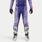 Alpinestars 2024 Techstar Ocuri crossbroek, motorcross broek, paars met felle oranje accenten, witte logo's, gedragen met witte motorcrosslaarzen en zwarte handschoenen, duurzame race-pasvorm voor motorcross