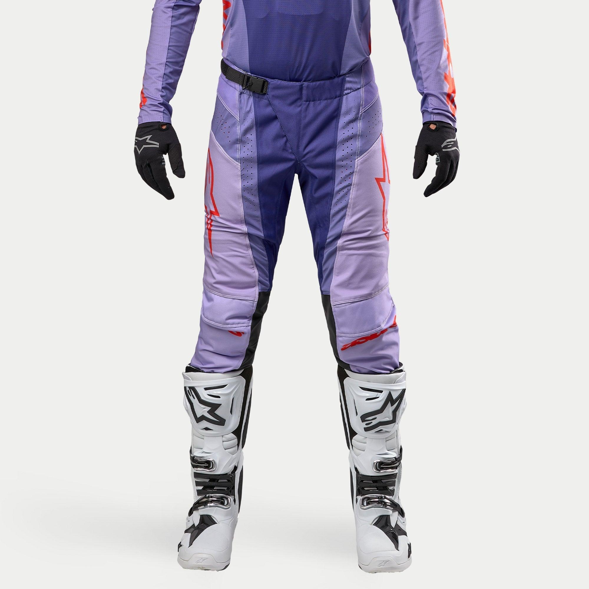 Alpinestars 2024 Techstar Ocuri crossbroek, motorcross broek, paars met felle oranje accenten, witte logo's, gedragen met witte motorcrosslaarzen en zwarte handschoenen, duurzame race-pasvorm voor motorcross