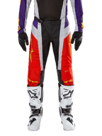 Alpinestars 2024 Techstar Ocuri crossbroek, motorcross broek, fel oranje, paars en zwart, gedragen met bijpassende jersey, zwarte handschoenen en witte laarzen, voorzien van opvallende oranje voorpanelen, paarse taille-accenten en geperforeerde grijze delen, technisch ontwerp voor off-road racen