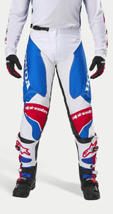 Alpinestars Honda Racer Iconic Pants, motorcross broek, wit, helderblauw en helderrood, met grote Honda-branding op de zijpanelen en het Alpinestars-logo op de knieën, gedragen met bijpassende jersey, zwarte handschoenen en motorcrosslaarzen, ontworpen voor off-road raceprestaties.
