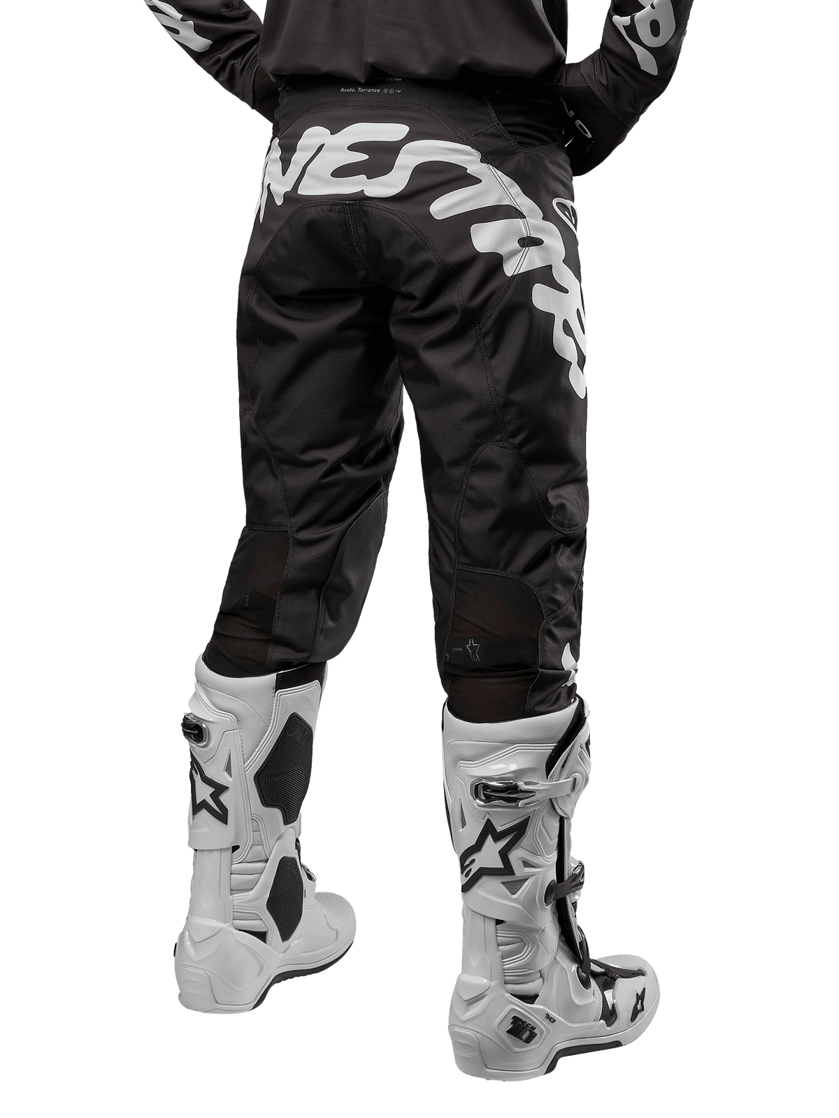 Alpinestars 2024 Racer Hana crossbroek, motorcross broek, zwart met grote witte grafische tekst op de achterzijde, achteraanzicht van een rijder met witte motorcrosslaarzen, duurzaam en technisch materiaal voor off-road rijden