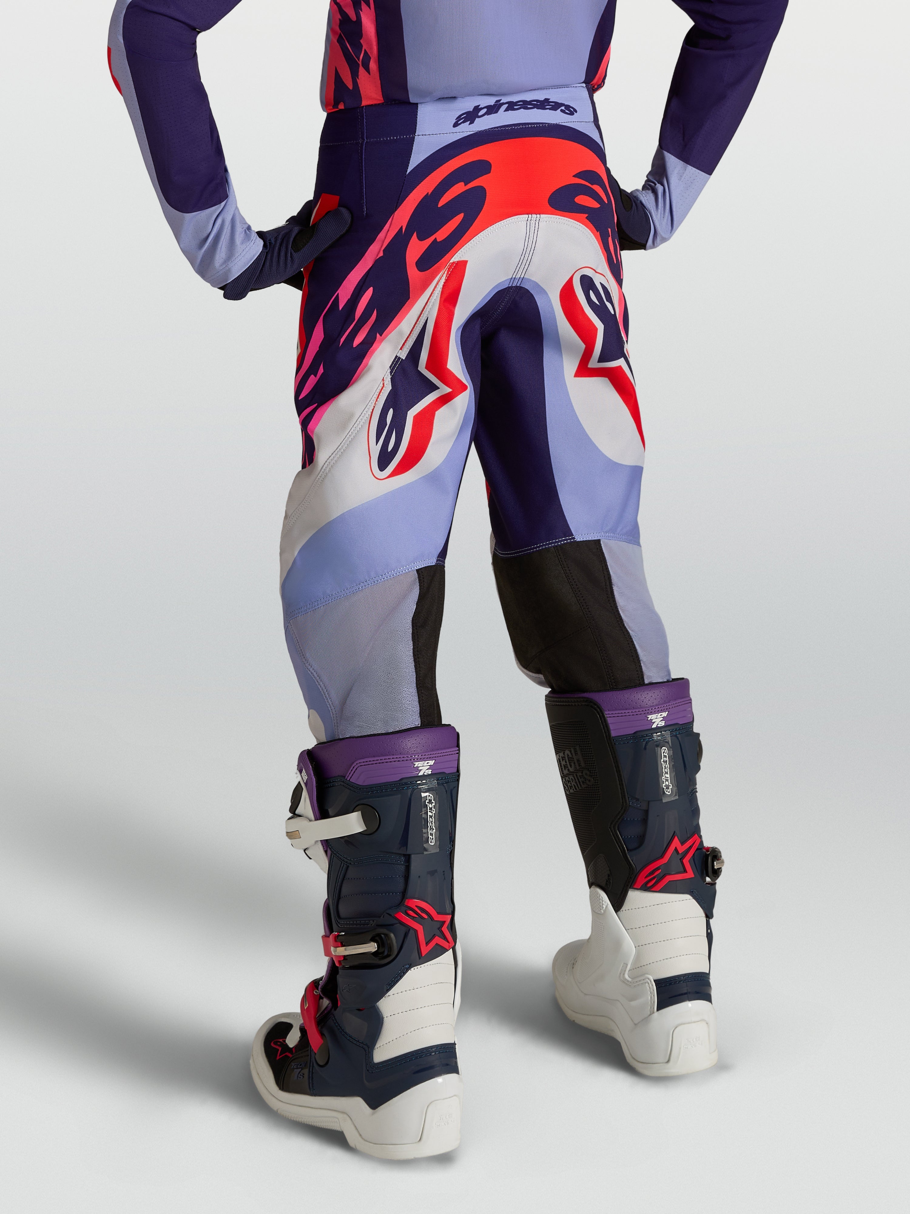 Alpinestars Jeugd Supertech Dyna broek, motorcrossbroek voor kinderen, paars en fluo roze, van duurzaam stretch rip-stop textiel, achteraanzicht op model met bijpassende uitrusting.