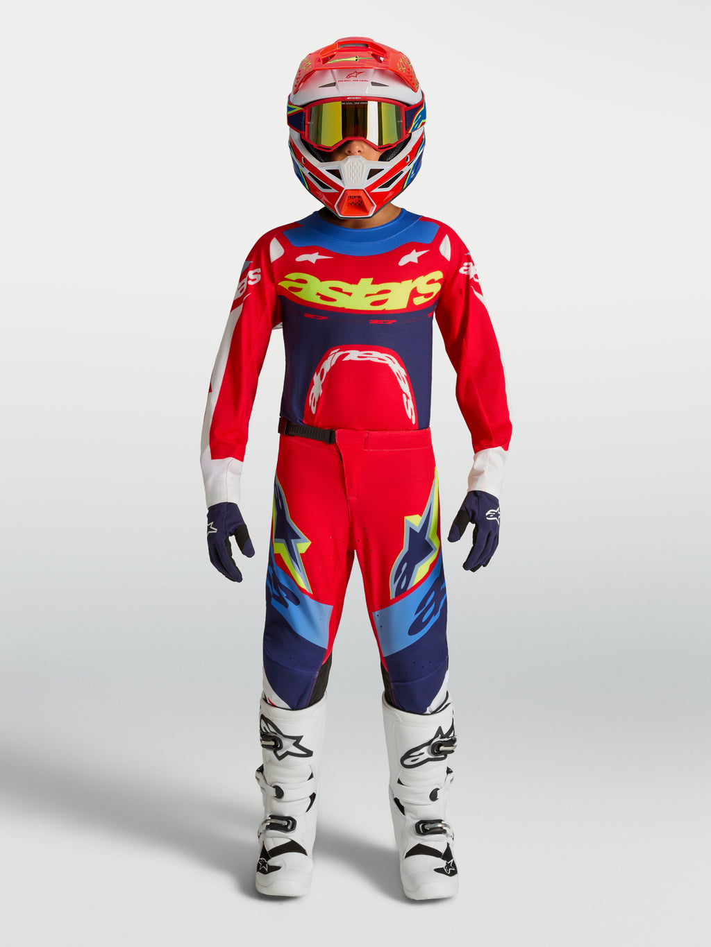 Alpinestars Jeugd Supertech Dyna broek, motocrossuitrusting in rood en marineblauw met witte motorlaarzen en helm.