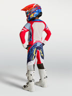 Alpinestars jeugd Supertech Dyna broek in rood, wit en blauw, achteraanzicht van een jonge rijder met witte motorlaarzen.