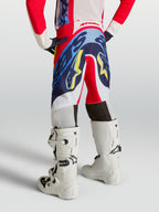 Alpinestars jeugd Supertech Dyna broek, motocrossbroek voor jonge rijders, achteraanzicht, rood, navy blauw en wit, gedragen met witte motorlaarzen, professionele off-road race-uitrusting.