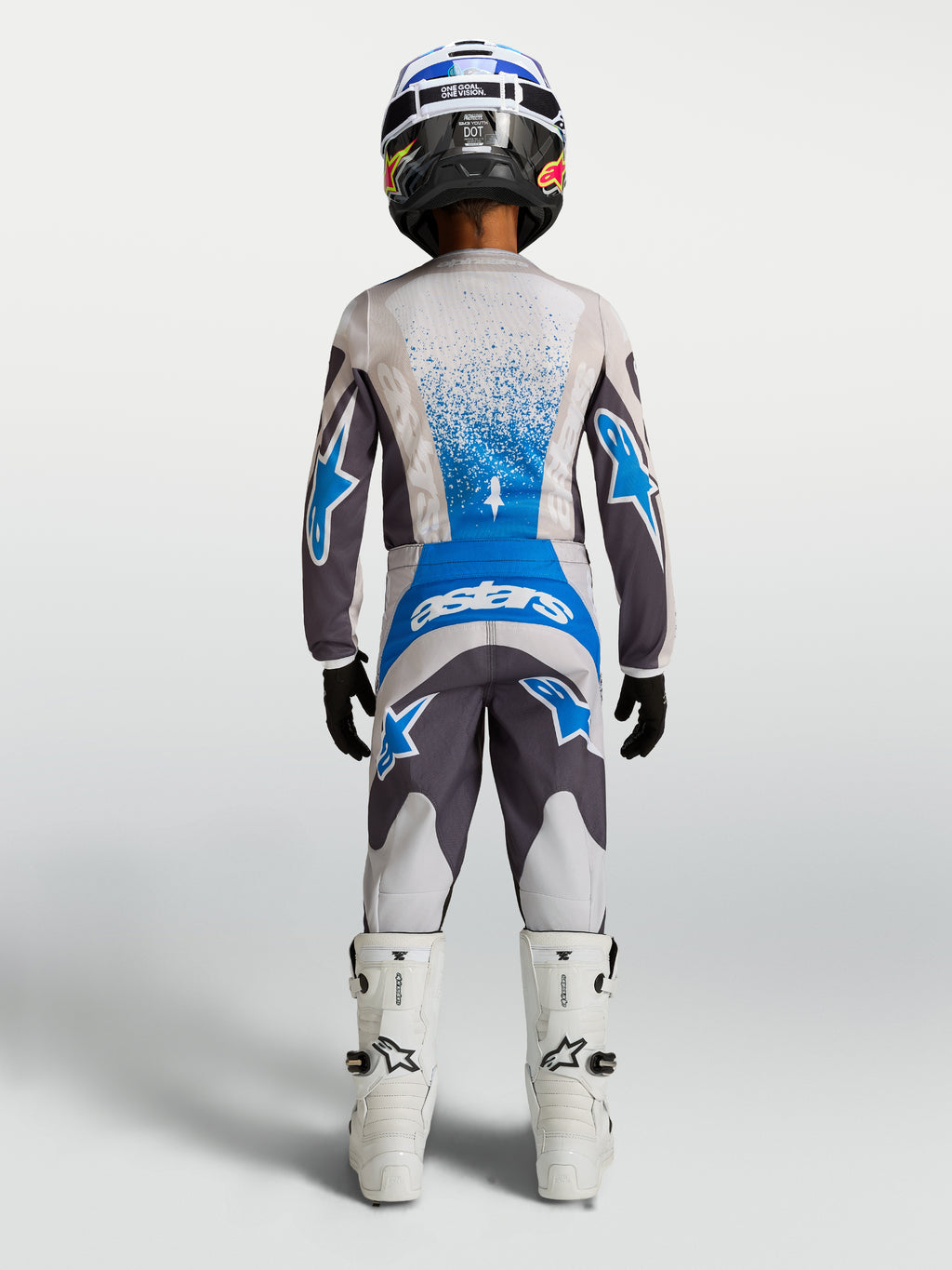 Alpinestars Jeugd Fluid Drag broek, motorcross off-road uitrusting voor jeugd, grijs en blauw, achteraanzicht op model met bijpassende jersey en witte motorlaarzen.