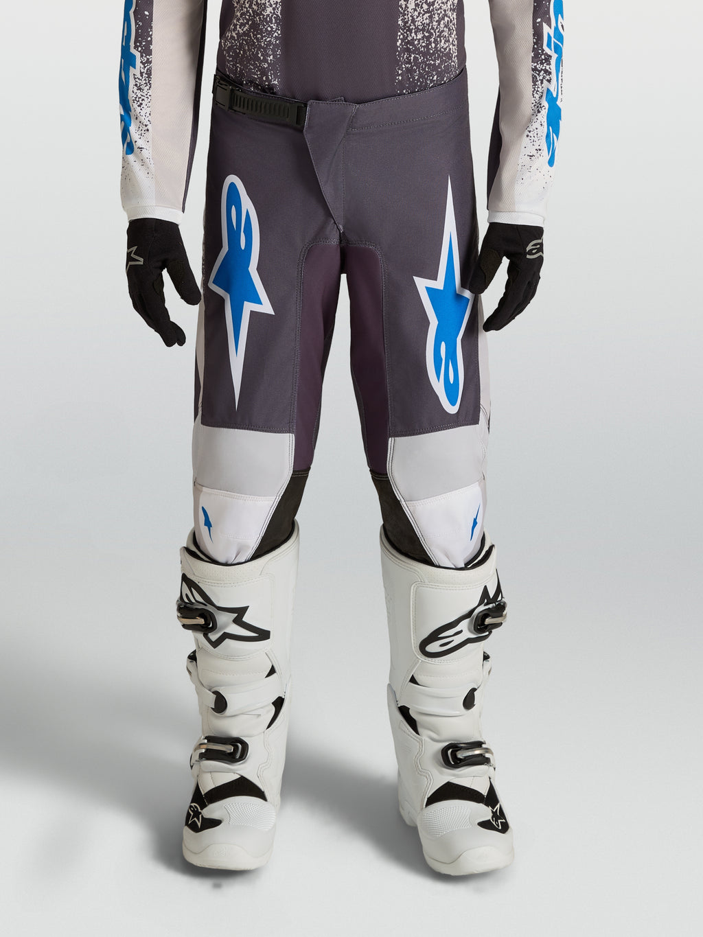 Alpinestars Jeugd Fluid Drag broek 2027, motorcrossbroek, grijs en blauw, 600D polystof met versterkte knieën, gedragen met witte motorlaarzen.