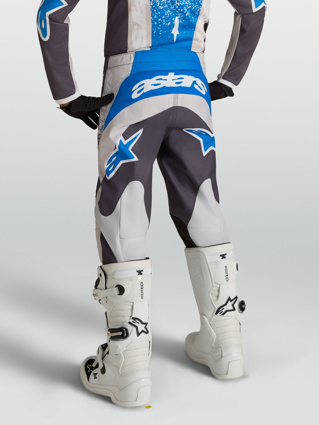 Alpinestars jeugd Fluid Drag broek in grijs en blauw, motocross-uitrusting van achteren met witte laarzen.