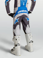 Alpinestars jeugd Fluid Drag broek in grijs en blauw, motocross-uitrusting van achteren met witte laarzen.