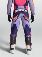 Alpinestars Jeugd Fluid Hunt broek, motocrossbroek voor off-road rijden, paars en roze, duurzame polystof constructie met stretchpanelen, model van achteren gezien met motorlaarzen.