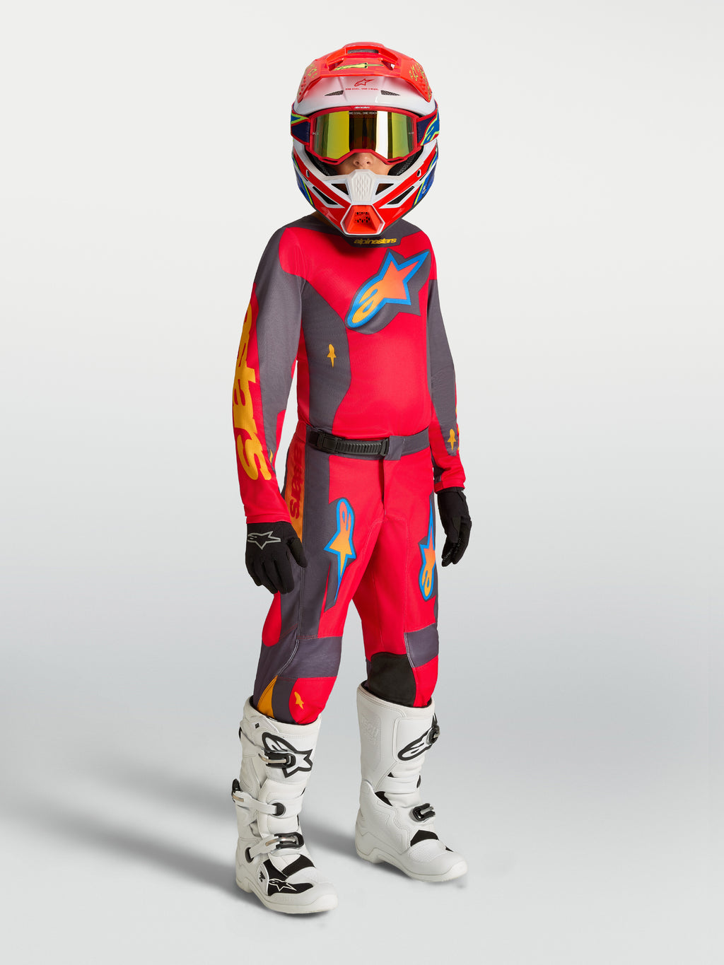 Alpinestars Jeugd Fluid Hunt broek, rood en grijs motocross-tenue op model met bijpassende jersey en witte laarzen.