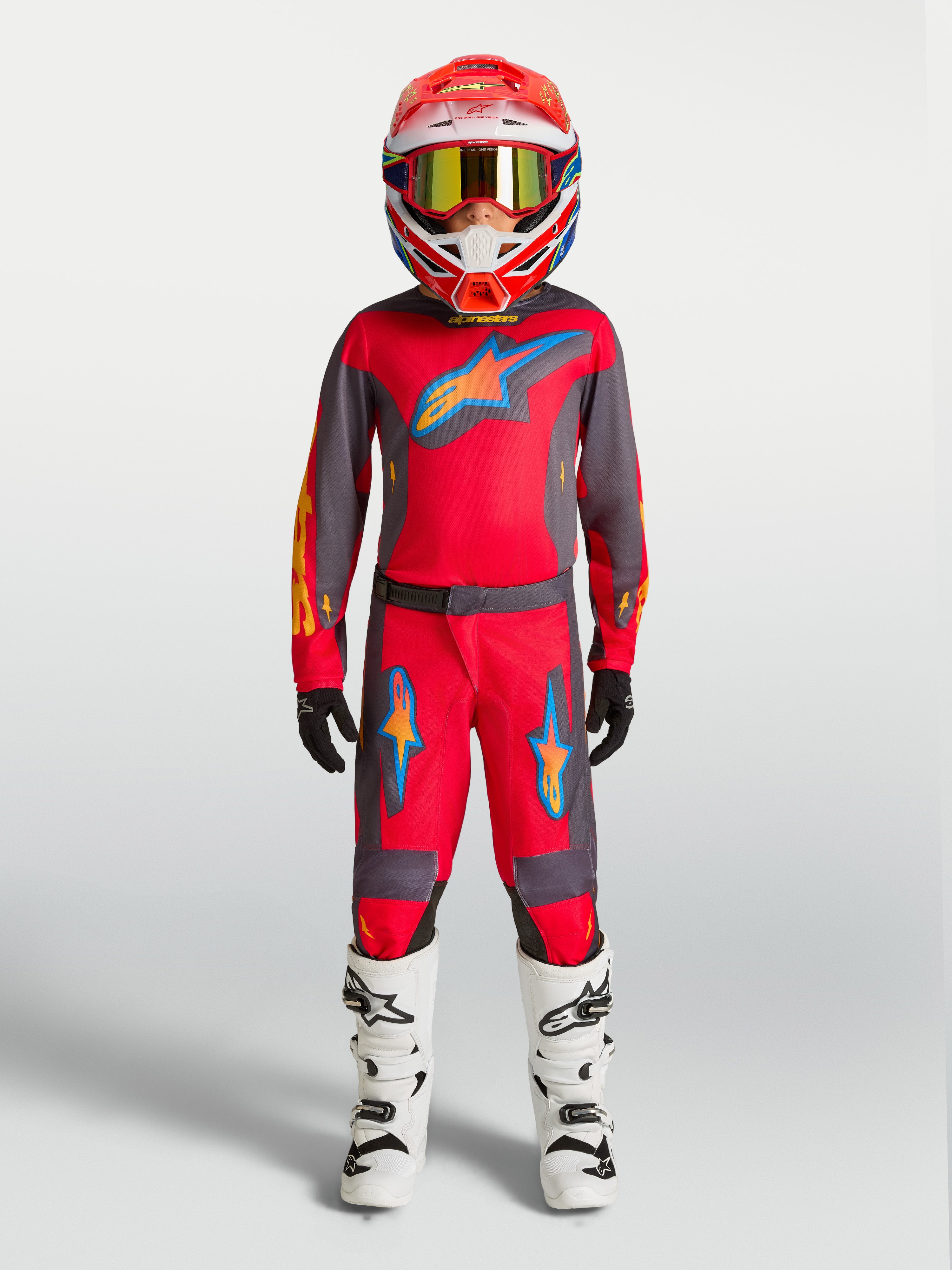 Alpinestars Jeugd Fluid Hunt broek, rode en grijze motorcrossbroek voor kinderen, sportieve pasvorm, gedragen met witte laarzen.