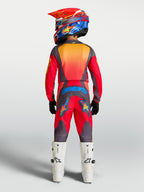 Alpinestars Jeugd Fluid Hunt broek, rode en grijze motocrossbroek, achterzijde van jonge rijder met witte motorlaarzen.