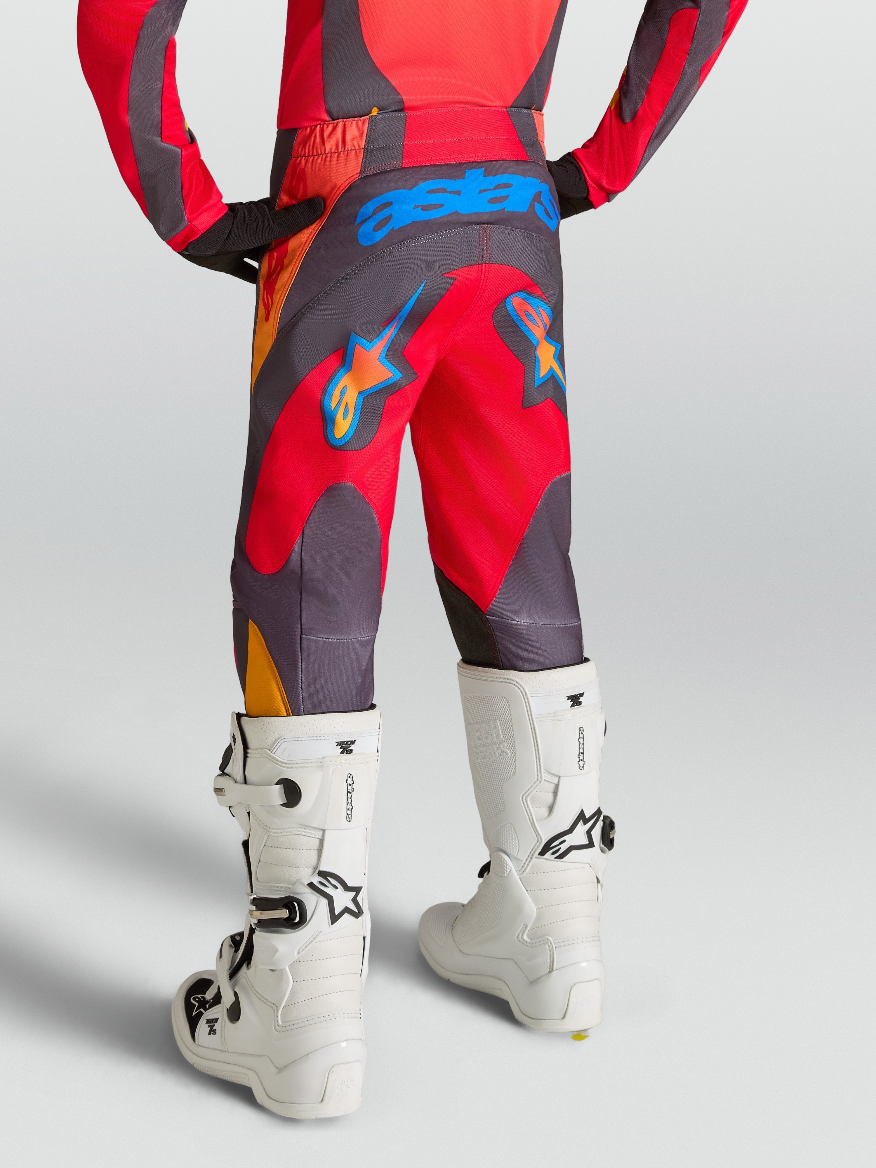 Alpinestars Jeugd Fluid Hunt broek, motorcrossbroek voor off-road rijden, rood en grijs, duurzaam 600D-zitvlak, achteraanzicht op model met witte motorlaarzen.