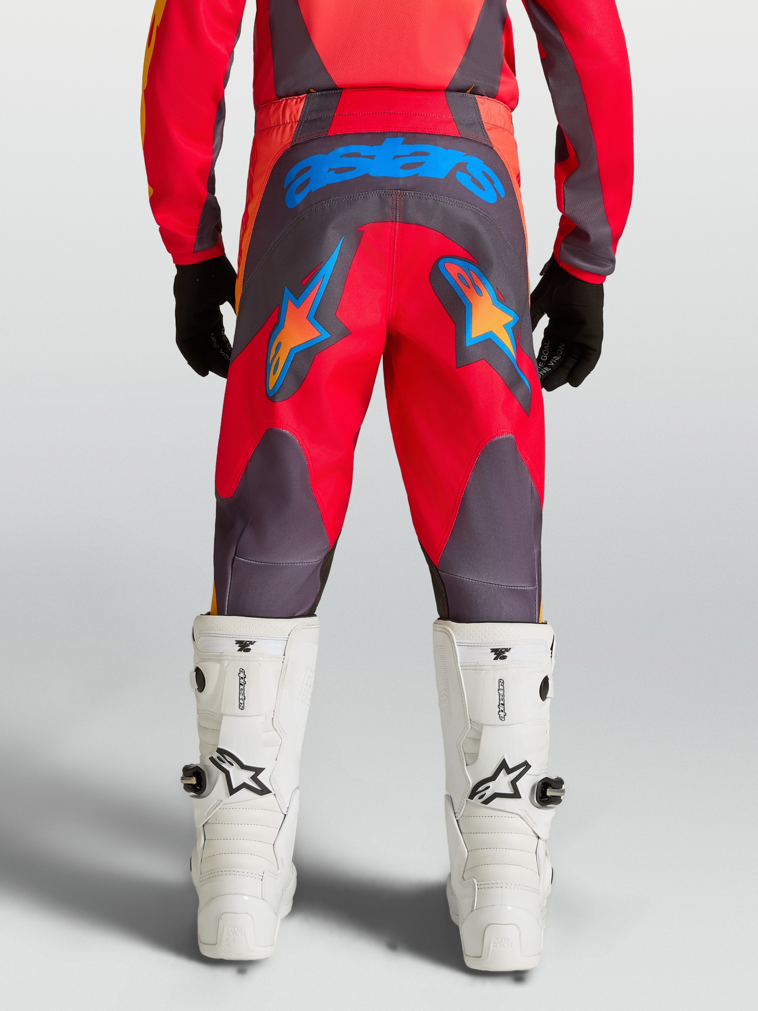 Alpinestars Jeugd Fluid Hunt broek, rood en grijze motocrossbroek met blauwe ster-graphics en 600D-zitvlak, achteraanzicht.