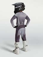 Alpinestars Jeugd Fluid Amber broek, grijze en paarse sport-fit motorcrossuitrusting met witte motorlaarzen.