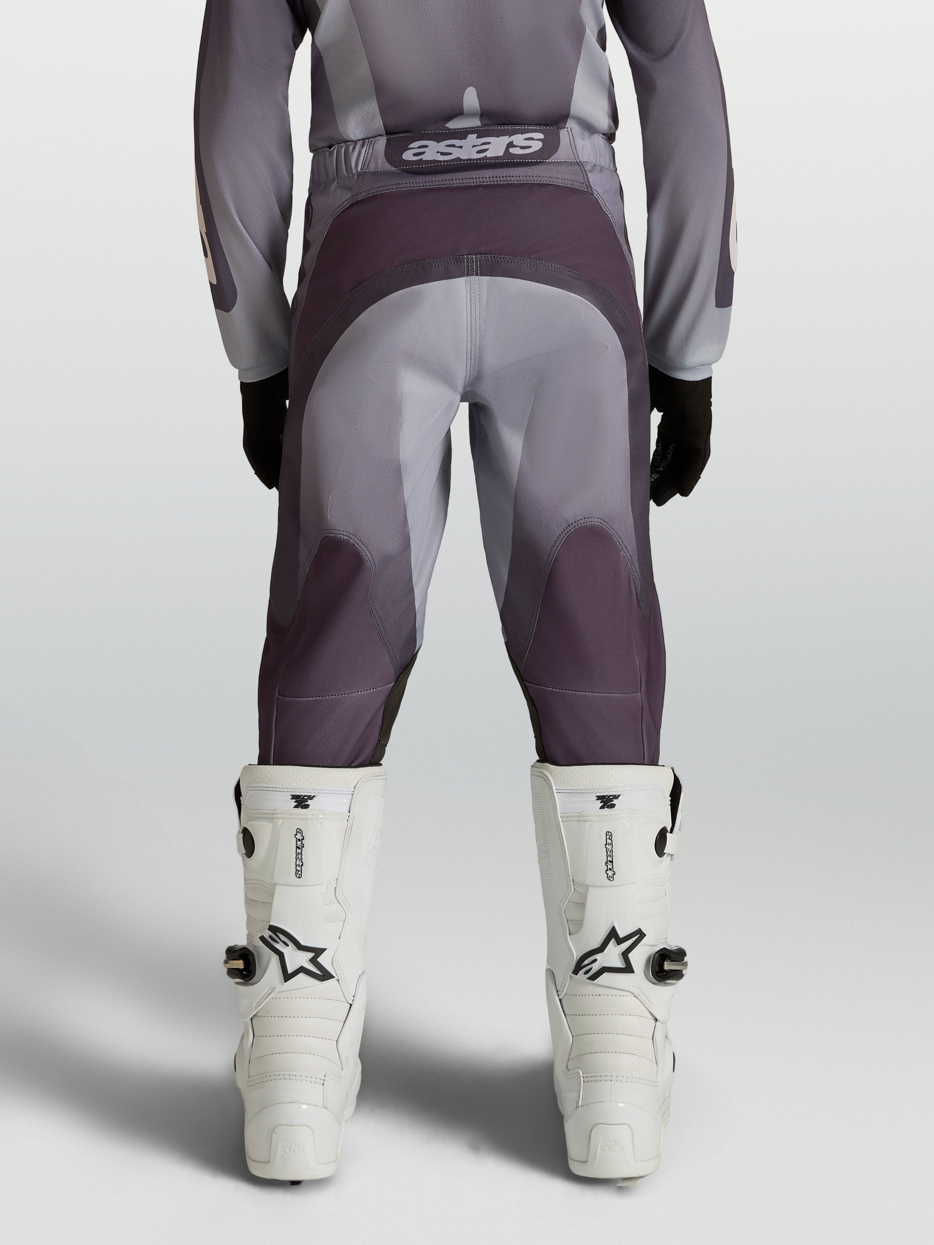 Alpinestars Jeugd Fluid Amber broek, motocrossbroek voor terreinrijden, grijs en zand, achteraanzicht met witte motorlaarzen.