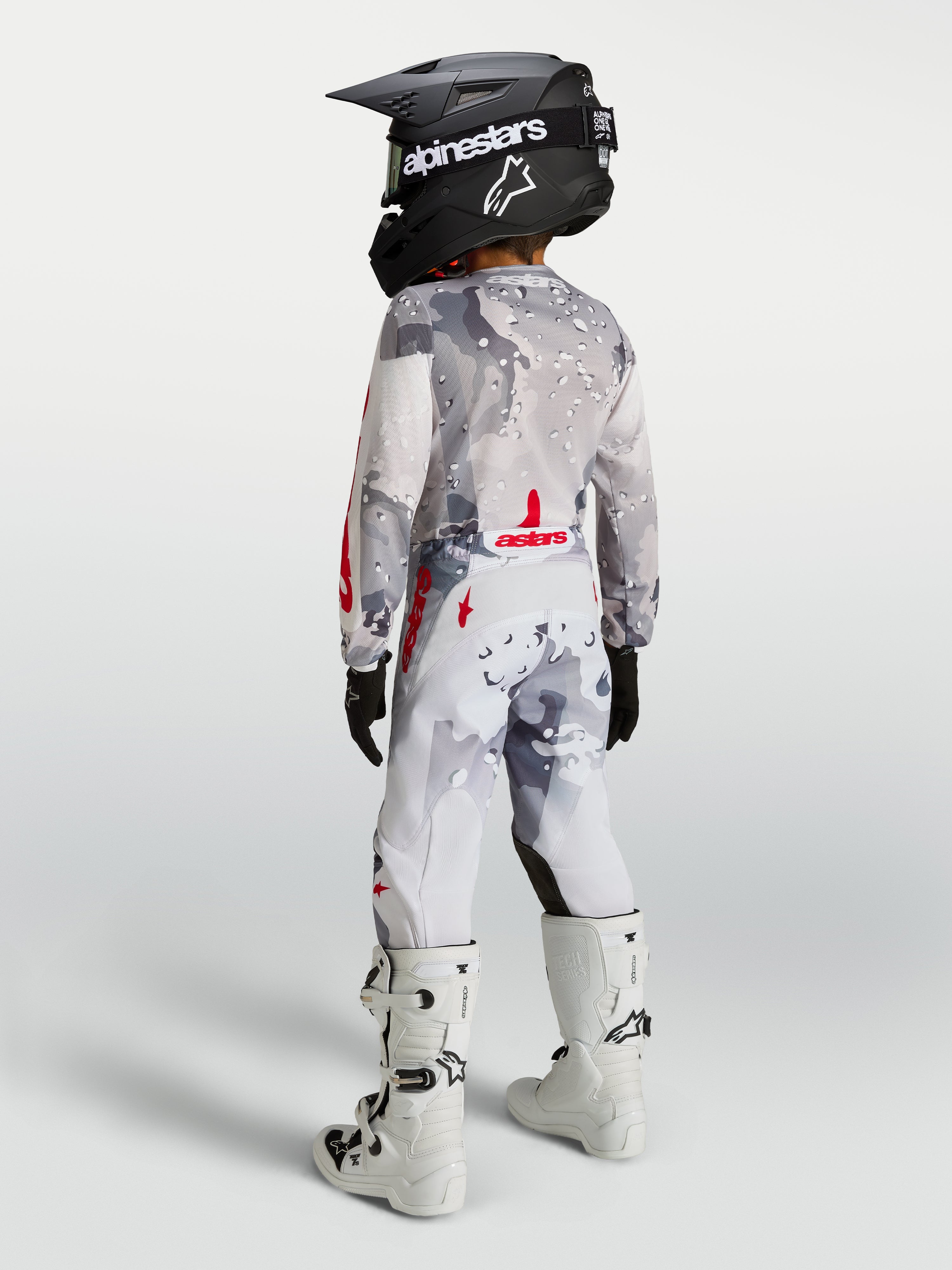 Alpinestars Jeugd Fluid Lone broek, grijs camo en wit met rood, motocrossbroek op een jeugdrijder van achteren.