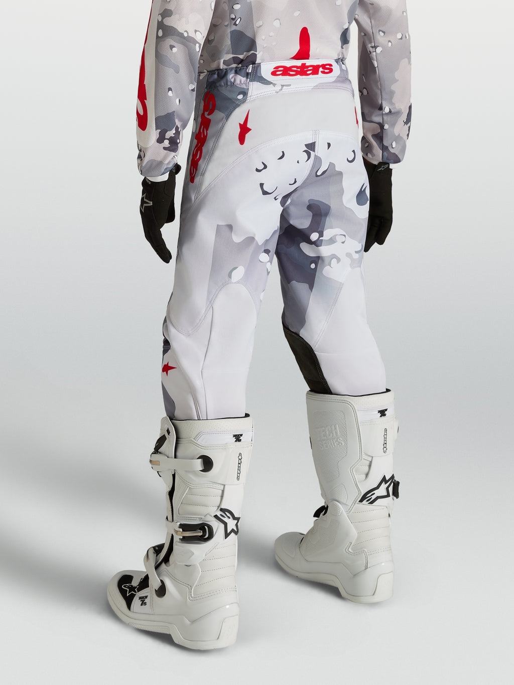 Alpinestars Jeugd Fluid Lone broek 2027, motorcrossbroek in grijs camo en rood, gedragen met witte motorlaarzen.