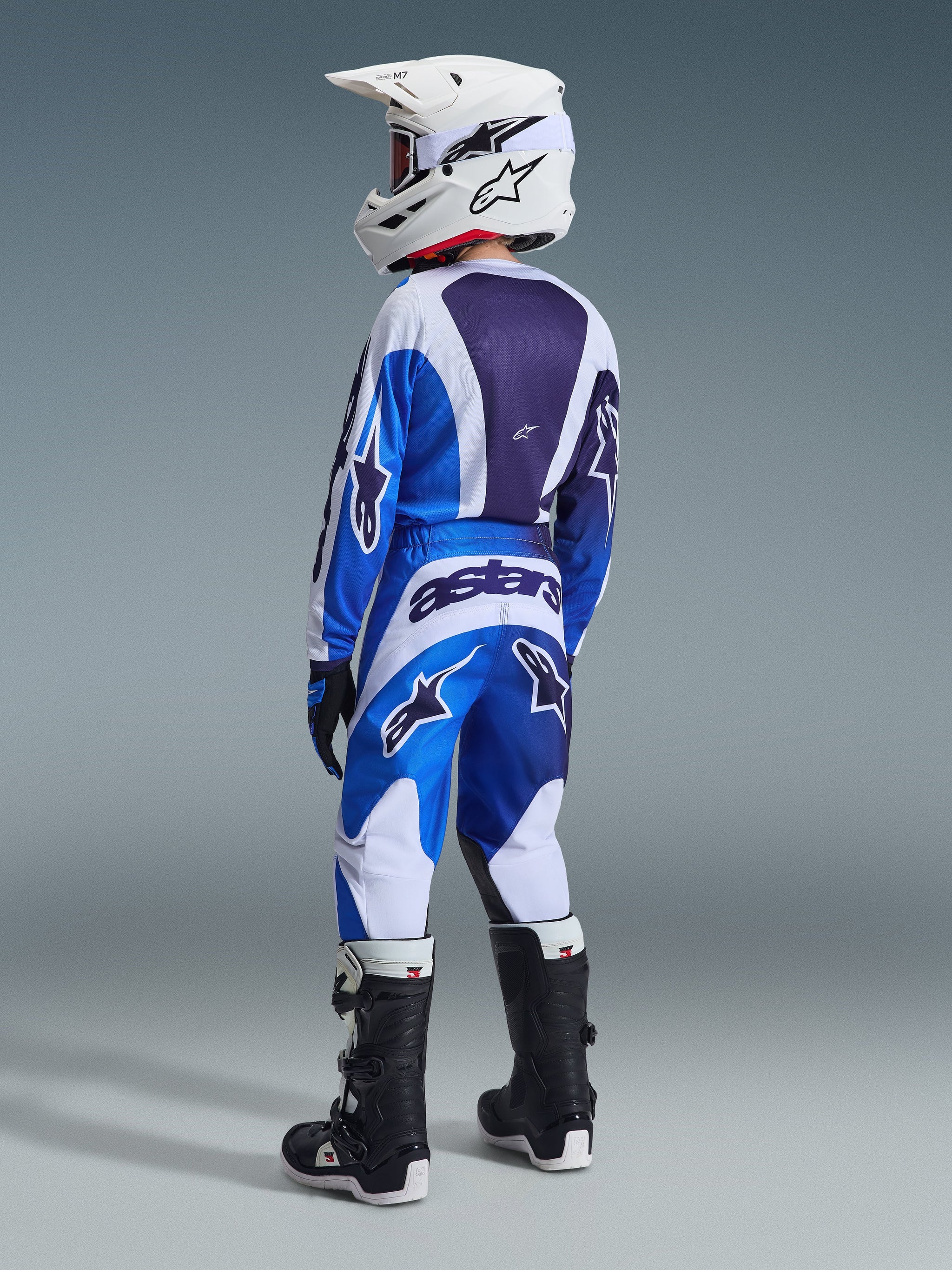 Alpinestars 2026 Youth Fluid Portl Pants, Motocross Pants, UCLA Blue and White, shown from a rear view on a rider wearing a matching jersey, white helmet, and black and white boots, featuring bold 'astars' branding across the back.