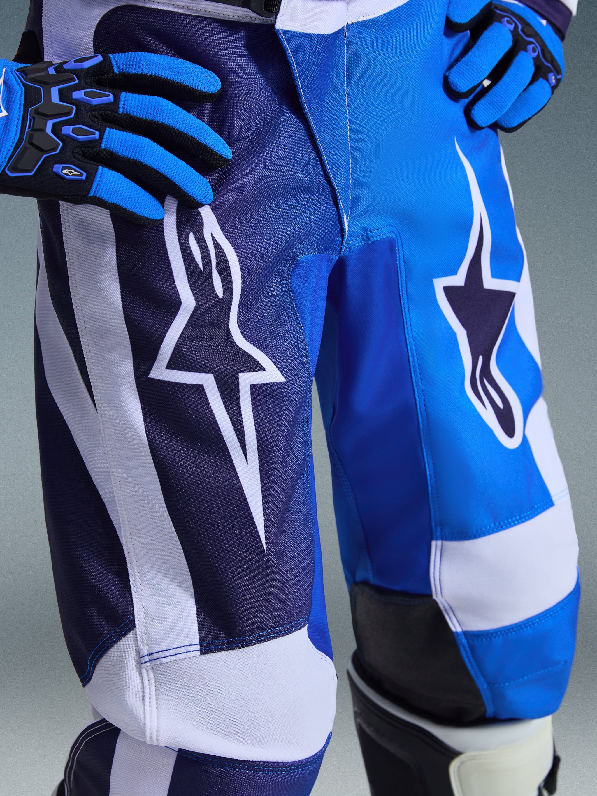 Alpinestars 2026 Youth Fluid Portl Pants, Motocross Pants, UCLA Blue and White, close-up view of a rider wearing the pants with hands on hips and blue and black gloves, featuring large white star logos and multi-toned blue panels, durable construction for off-road racing
