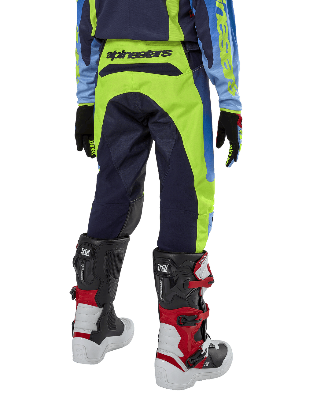 Alpinestars Youth 2024 Racer Hoen motorcrossbroek, fluogeel en donkerblauw, achteraanzicht met opvallende Alpinestars-branding op de tailleband, gedragen met zwart-rode Tech Series laarzen en bijpassende jersey, duurzame sportieve pasvorm voor off-road rijden