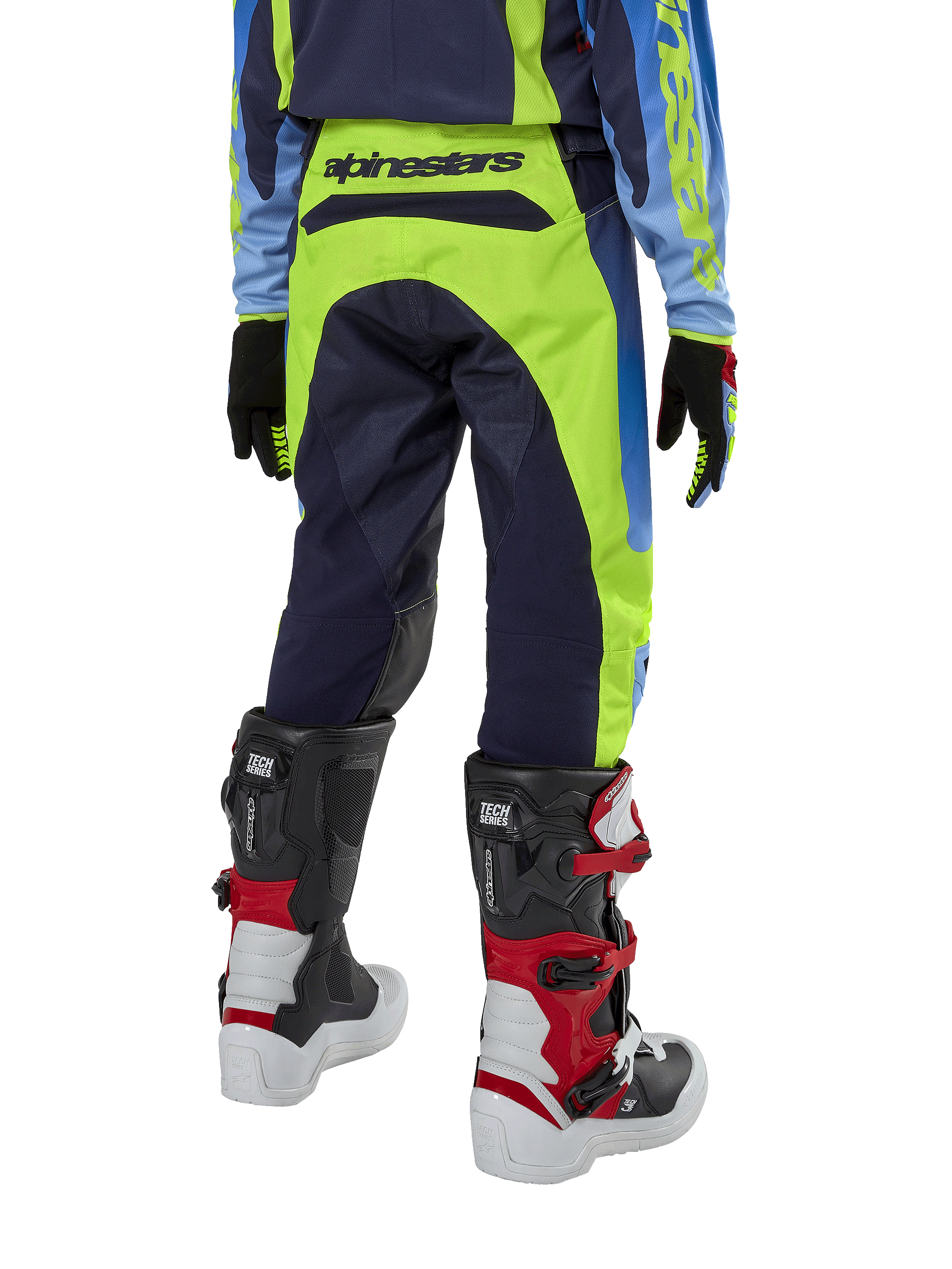 Alpinestars Youth 2024 Racer Hoen motorcrossbroek, fluogeel en donkerblauw, achteraanzicht met opvallende Alpinestars-branding op de tailleband, gedragen met zwart-rode Tech Series laarzen en bijpassende jersey, duurzame sportieve pasvorm voor off-road rijden