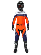 Motorcrossrijder in volledige Alpinestars Pro-Dura uitrusting, navy, feloranje en wit jersey, bijpassende oranje en navy broek, zwarte motorcrosslaarzen met witte logo's, zwarte helm en handschoenen, gecoördineerde outfit voor off-road racen