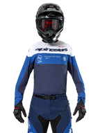 Alpinestars Pro-Dura Jersey, motocross- en enduroshirt, marineblauw, helderblauw en wit, gedragen met bijpassende marineblauwe broek, zwarte handschoenen en helm, voorzien van merklogo op de borst en lasergesneden ventilatie voor off-road motorraces