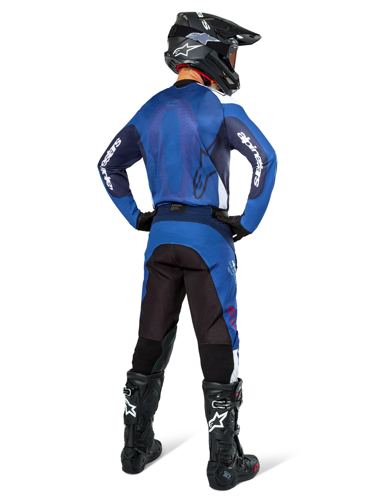 Motocrossrijder van achteren die een Alpinestars Pro-Dura Jersey in Navy en helderblauw draagt, met bijpassende blauwe en zwarte broek, zwarte motorcrosshelm met goggle en zwarte laarzen, toont een gecoördineerde off-road race-outfit