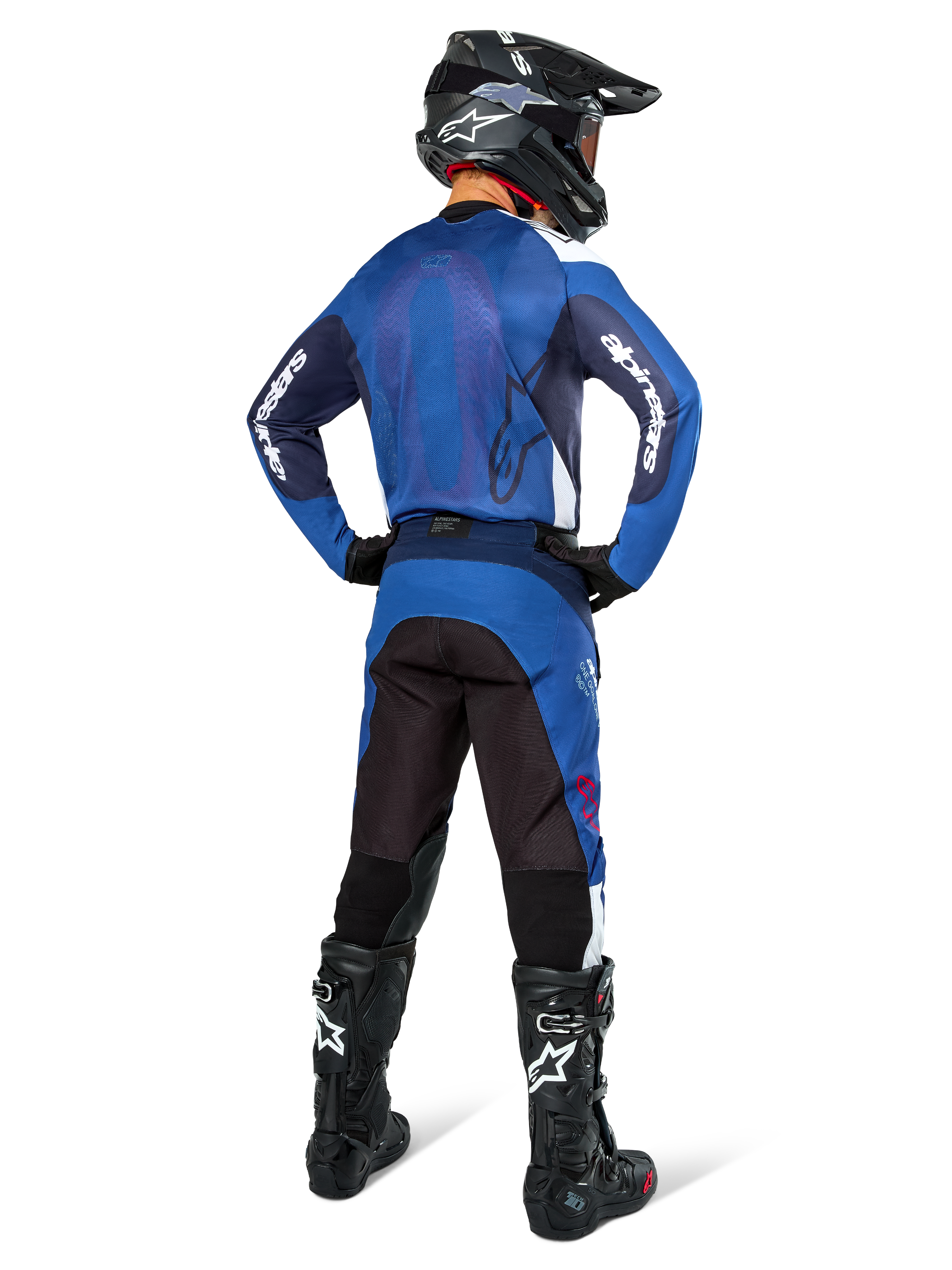 Motocrossrijder van achteren die een Alpinestars Pro-Dura Jersey in Navy en helderblauw draagt, met bijpassende blauwe en zwarte broek, zwarte motorcrosshelm met goggle en zwarte laarzen, toont een gecoördineerde off-road race-outfit