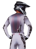 Motocrosser van achteren die de Alpinestars 2025 Supertech Maker Jersey draagt, zilver en zwart met een rood mesh rugpaneel en zwarte logo's op de mouwen, gecombineerd met een bijpassende motorcrossbroek en een zwart-witte helm, professionele off-road race-uitrusting